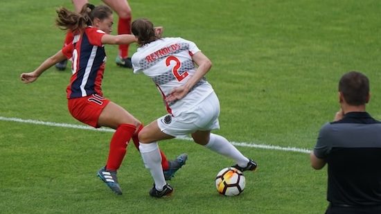 two female athletes playing soccer on field